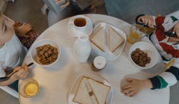 Children enjoying a breakfast with cereal and sliced bread at a cozy indoor dining table.