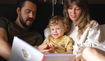 A happy family reading together, featuring parents and their smiling child enjoying a book indoors.