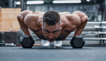 Fit man doing push-ups on hex dumbbells in a modern gym setting.