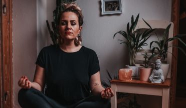 Peaceful female in black clothes and stylish earring meditating during yoga session at home